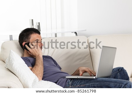 beautiful young man on sofa with computer and phone