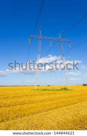 high-voltage lines on harvested wheat field with blue sky in summer