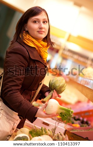Beautiful young woman buying artichokes and fennel bulbs at market