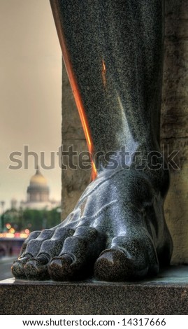 Foot of granite telamon with Saint-Isaac\'s Cathedral in the background. Saint-Petersburg, Russia.