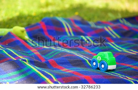 Summer picnic with a child. Small toy car on a checkered blanket laid on the grass for children games