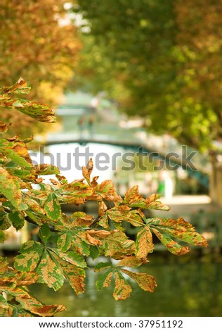 Autumn in Paris. View of beautiful canal Saint-Martin with its pedestrian bridge and a couple on it through the autumn leaves