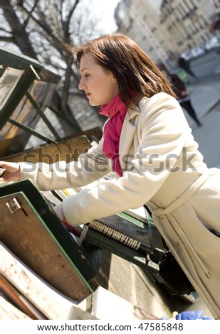 Beautiful woman in Paris selecting a book in an outdoor bookseller box