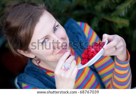 Young girl in bright clothes eating raspberry