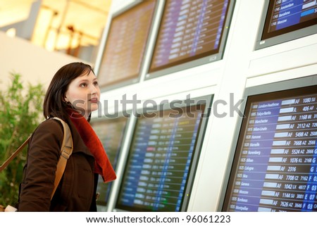Beautiful young tourist in the airport looking at the flight board