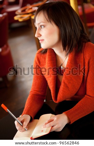 Beautiful young woman writing something in her personal organizer in cafe