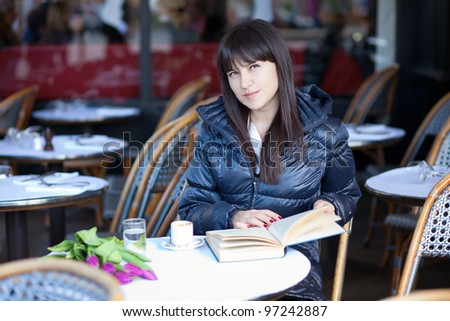 Dark-haired beautiful woman with book in Parisian street cafe