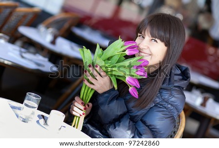 Smiling brunette lady with beautiful tulips in Parisian street cafe