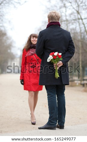Happy couple having a date, man is going to offer flowers to his girlfriend