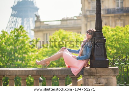 Beautiful girl in pink dress sitting near the Eiffel tower in Paris