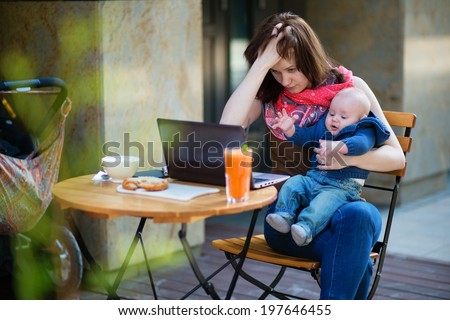 Tired young mother working oh her laptop and holding 4-month son