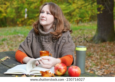 Girl having a picnic in park on a fall day and reading a book