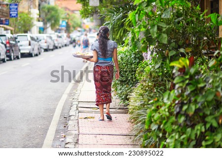 Balinese woman walking down the street in Ubud carrying plate with offerings to gods in her hand