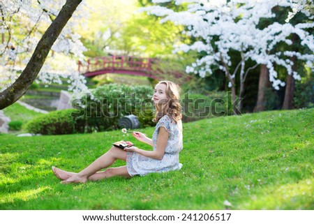 Beautiful young girl eating sushi in cherry blossom garden on a spring day