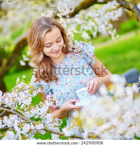 Beautiful young woman in cherry blossom garden with cup of tea or coffee on a spring day
