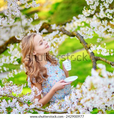 Beautiful young woman in cherry blossom garden with cup of tea or coffee on a spring day