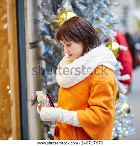 Worried young woman holding purse with Russian roubles in shopping mall decorated for Christmas, financial crisis in Russia concept