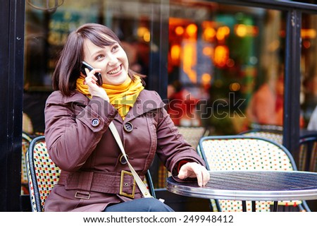 Happy young girl talking on cell phone in Parisian street cafe