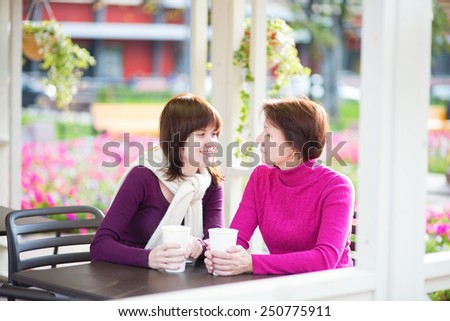 Beautiful middle aged woman with her grown up daughter spending time together and talking in an outdoor cafe