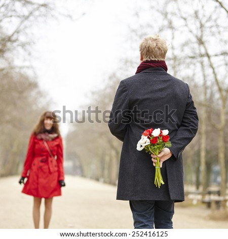 Happy couple having a date, man is going to offer flowers to his girlfriend