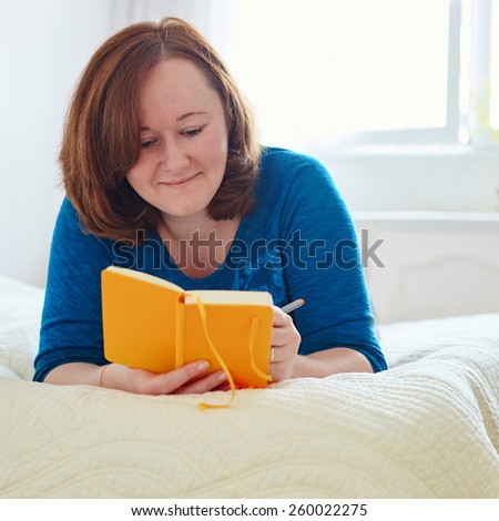 Girl lying on the bad and writing into diary or planning her day