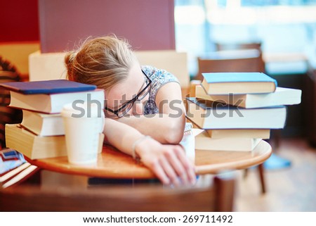 Beautiful young student with lots of books, preparing for exams in a cafe and sleeping on the table tired. Shallow DOF