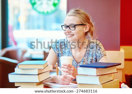 Beautiful young student with lots of books, studying or preparing for exams in a cafe. Shallow DOF