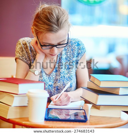 Beautiful young student with lots of books, studying or preparing for exams in a cafe. Shallow DOF