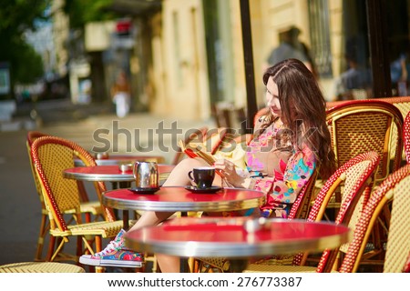 Beautiful young woman in Paris, drinking coffee in an outdoor cafe and reading book on a nice sunny day