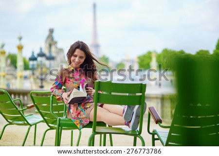 Young Parisian woman in the Tuileries garden, sitting on a chair and reading a book