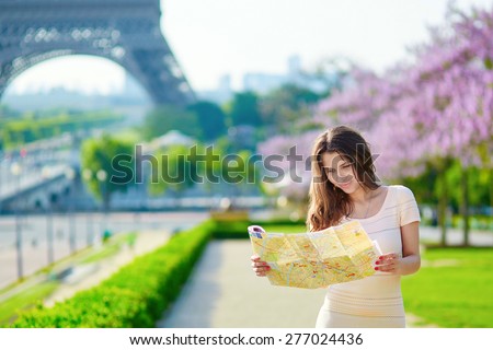 Young beautiful female tourist with map near the Eiffel tower in Paris, looking for the direction