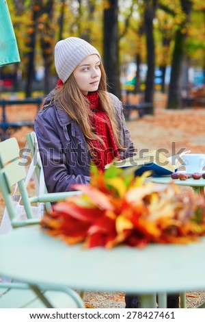 Girl reading a book in an outdoor cafe on a bright fall day in Paris