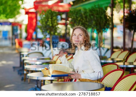 Beautiful young woman in Paris, drinking coffee in an outdoor cafe and reading book on a nice sunny day
