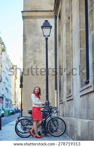 Beautiful young woman in red polka dot dress with a bicycle on a Parisian street