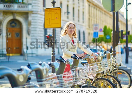 Beautiful young woman in red polka dot dress taking a bicycle for rent in Paris
