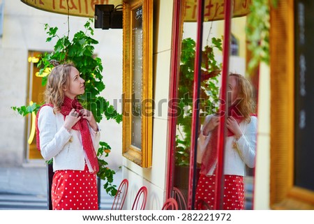 Beautiful young woman in red polka dot dress looking at the menu in a Parisian restaurant window