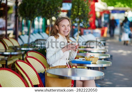 Beautiful young woman in Paris, drinking coffee in an outdoor cafe and using her mobile phone on a nice sunny day