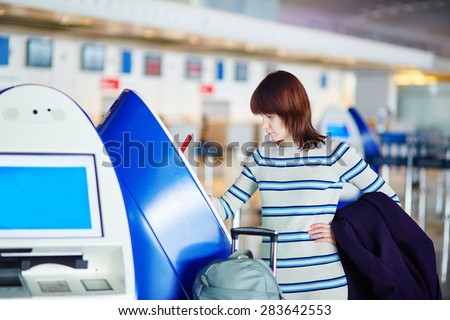 Young female passenger at the airport, doing self check-in at counter
