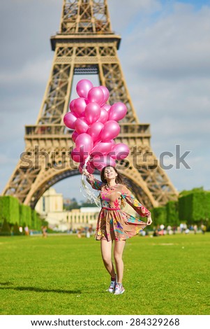 Beautiful young woman near the Eiffel tower in Paris with huge bunch of pink balloons, celebrating her birthday or other event
