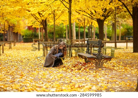 Beautiful young woman in Paris gathering fall leaves in park on a beautiful colorful autumn day
