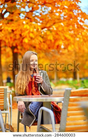 Beautiful young woman in a Parisian street cafe drinking hot wine on a beautiful colorful autumn day