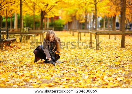 Beautiful young woman in Paris gathering fall leaves in park on a beautiful colorful autumn day