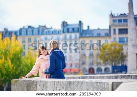 Young dating couple in Paris on a bright fall day, walking together by the Seine, colorful autumn leaves in the background