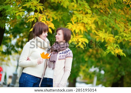 Mother and daughter together in park on a bright fall day, having fun, autumn leaves in the background