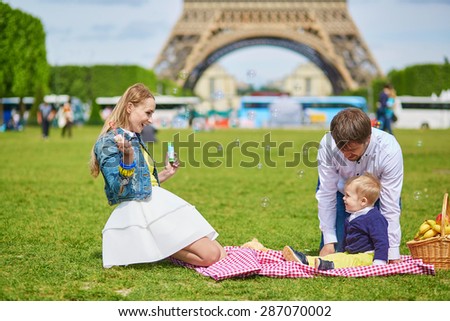Happy family of three, mother, father and little toddler boy, having picnic in Paris near the Eiffel tower and playing with bubbles