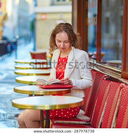 Beautiful young woman in red polka dot dress reading a book or planning her day in an outdoor cafe in Marais, Paris, France