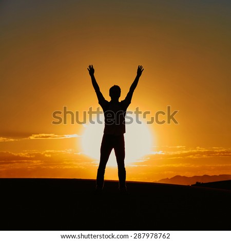 Silhouette of a man with his hands up during the sunset in Erg Chebby, Merzouga, Sahara desert situated in Morocco, Africa