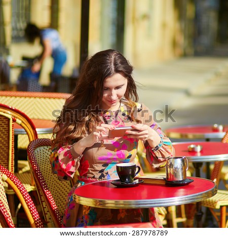 Beautiful young woman in a Parisian street cafe, taking photo of her coffee cup with mobile phone