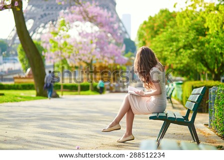 Beautiful young woman in Paris, near the Eiffel tower on a nice and sunny spring day, reading on the bench outdoors