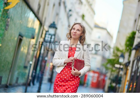 Beautiful young woman in red polka dot dress walking on a street of Marais in Paris, France